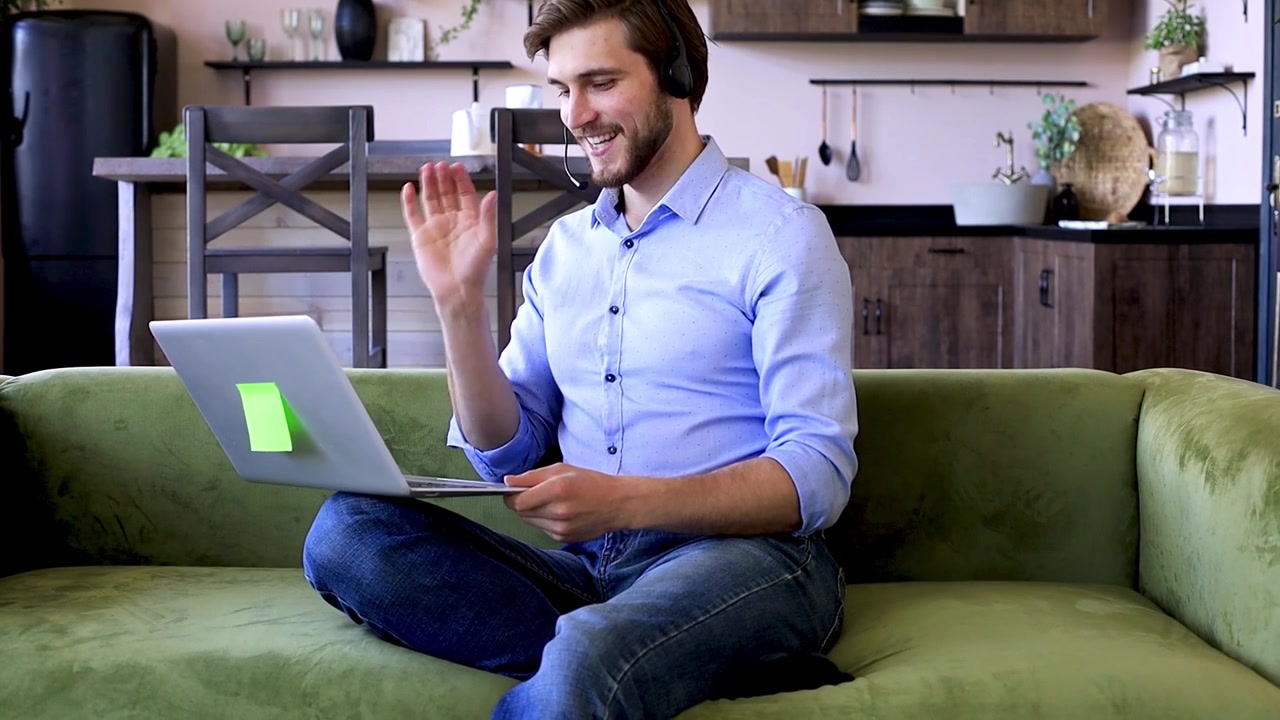 Jovem com fone de ouvido fazendo uma videochamada no laptop do sofá de casa.