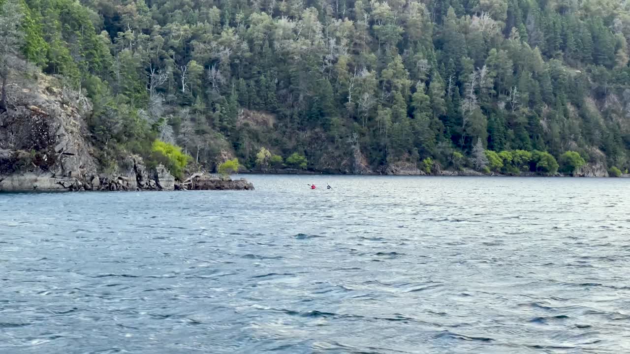 Kanu paddlers in Patagonia's scenic lake with lush forest and mountainous backdrop