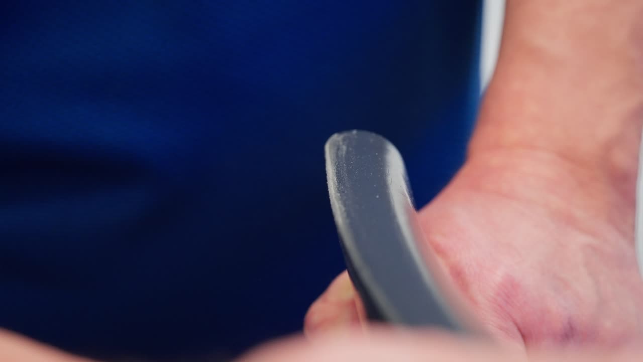 Man in blue shirt sands back of grey chair with sandpaper, wood exposed