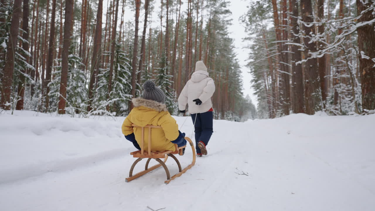 una donna corre nella foresta d'inverno e tira la slitta con il suo figlioletto per un felice fine settimana in famiglia.