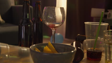 close up of messy table covered with empty wine glasses and beer bottles after house party