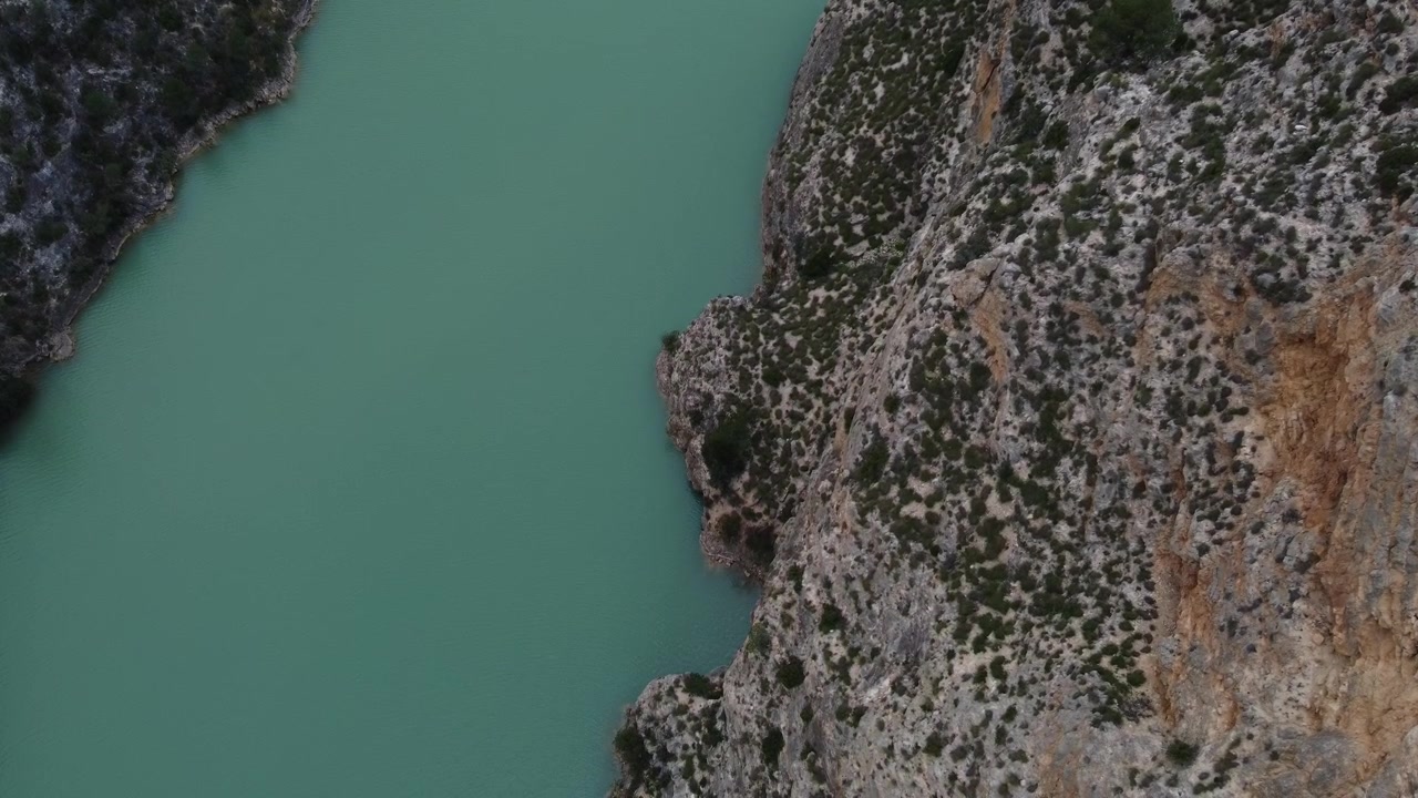 Discesa verticale di un drone 4K vicino a un'enorme scogliera rocciosa nella gola del fiume Júcar, Castiglia-La Mancia, Spagna, rivelando l'acqua turchese molto più in basso