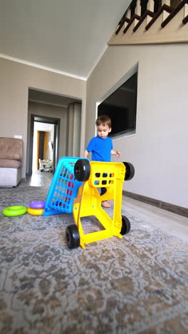 toddler boy wearing blue t-shirt turns around the toy cart. toys fall on the carpet from the trolley. vertical video.