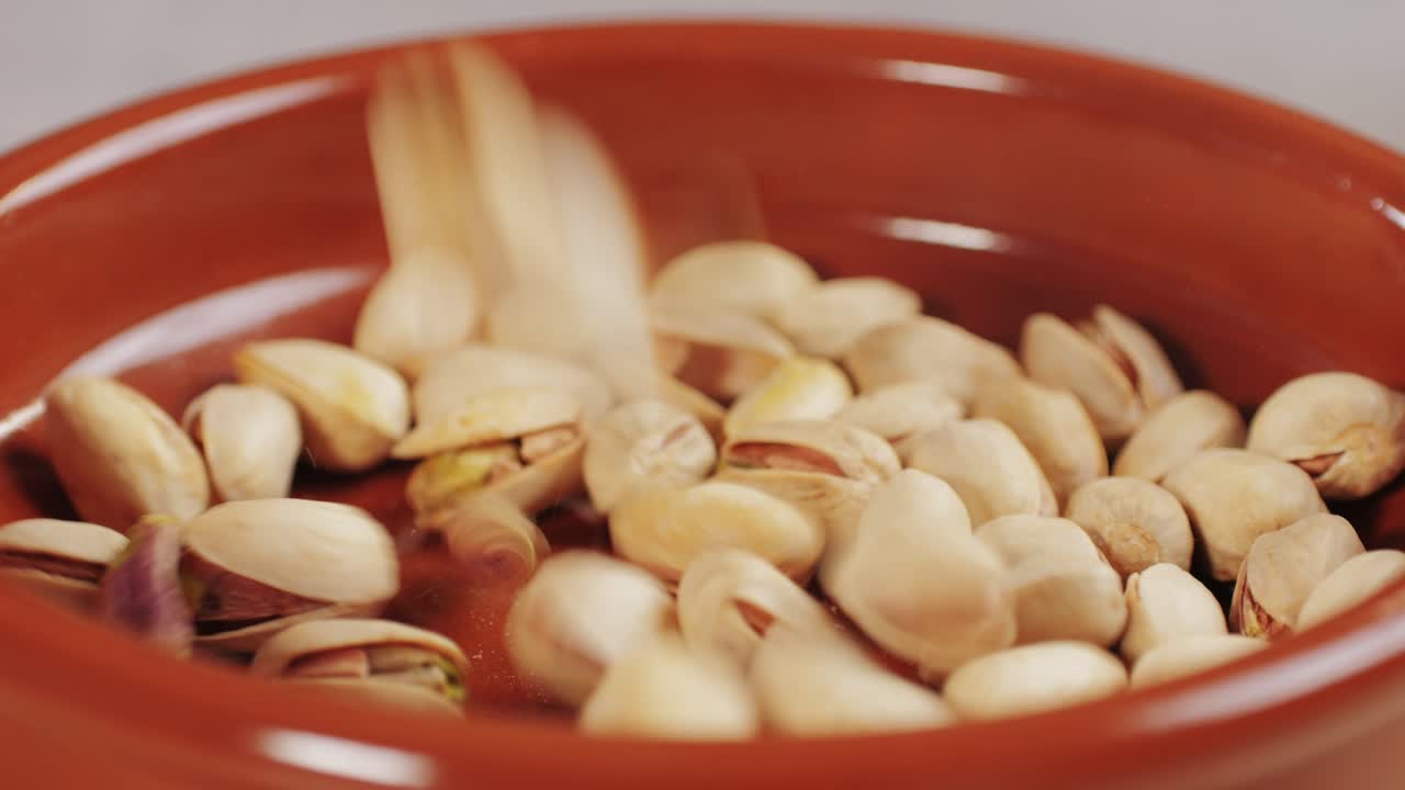 Salted pistachios falling down on red plate close-up macro. Nuts snacks for parties, fried crispy pistachios with cracked shells for beer