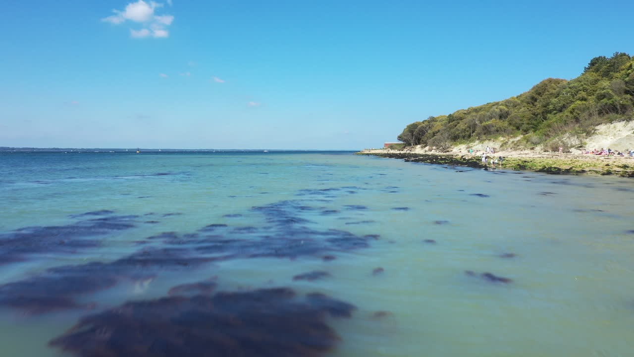 Aerial shot over blue sea water, starting low then rising, shot on a blue sky day