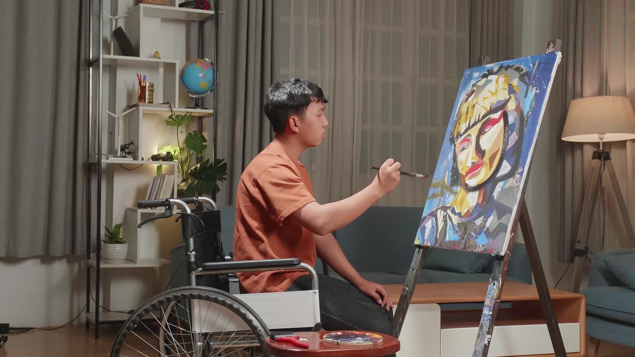 Side View Of An Asian Artist Boy In Wheelchair Holding Paintbrush Mixed Colour Thinking And Painting A Girl On The Canvas