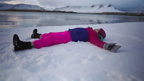 Happy girl lying on snow making angel figure in family holiday, winter vacations