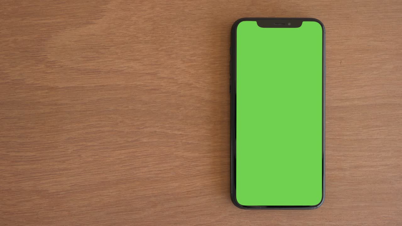 Smartphone posizionato su tavolo di legno, telefono con schermo verde, display ravvicinato di telefono cellulare con mockup, monitor Chroma Key, primo piano del cellulare su scrivania marrone, mockup smartphone, vista dall'alto con zoom