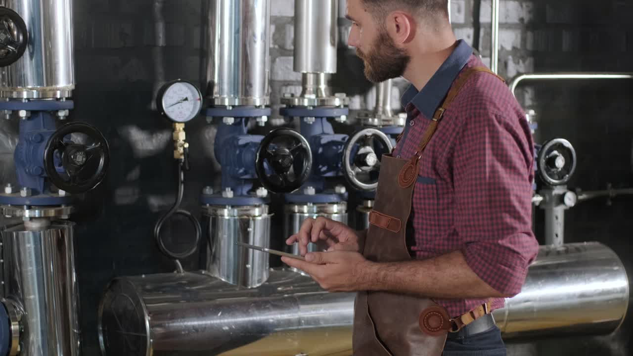 un joven cervecero con un delantal de cuero supervisa el proceso de fermentación de la cerveza en una fábrica de cerveza moderna