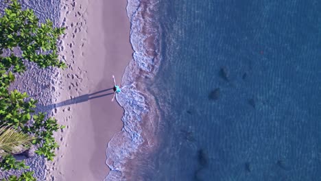 Woman-open-arms-with-dress-on-beach-in-water-makes-long-shadow