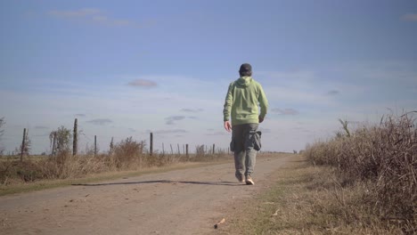 Rear-view-of-a-man-walking-away-from-the-camera-over-a-dirt-road-in-a-rural-setting