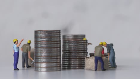 miniature workers working and piles of coins.