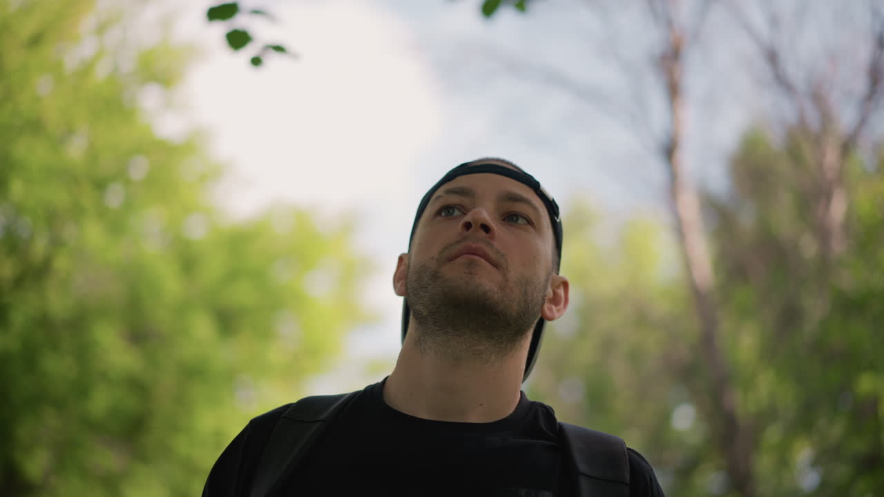 Persona che guarda il cielo, giovane con cappello osserva le cime degli alberi e il cielo immenso sopra di sé, giovane con cappello osserva attentamente le cime degli alberi e il cielo ampio da un ambiente boschivo ombreggiato