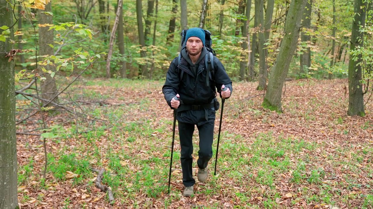 Uomo che fa escursioni in una foresta autunnale con zaino e bastoncini da trekking.