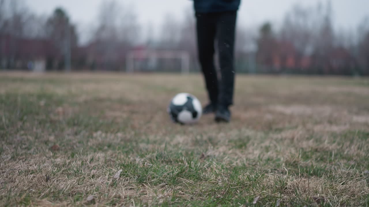 Blurred close-up of someone passing a football to another person who stops the ball, as he walks away, the background features a blur grassy field
