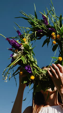 woman holding a vibrant floral wreath against a clear blue sky