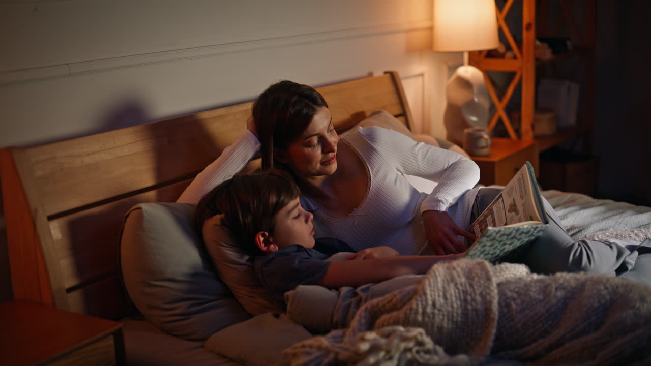 Mother read bedtime story adorable son lying together evening bedroom closeup