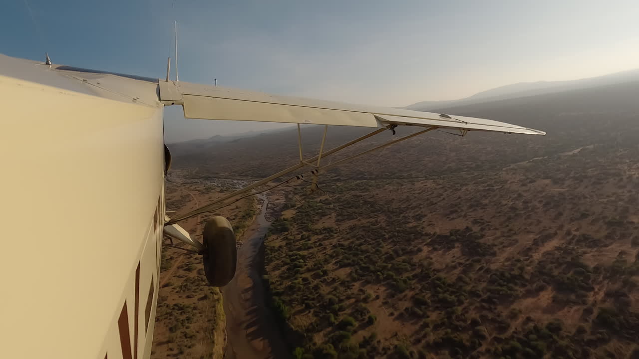 Seitenansicht eines kleinen Flugzeugs über Sträuchern, Fluss und Straße