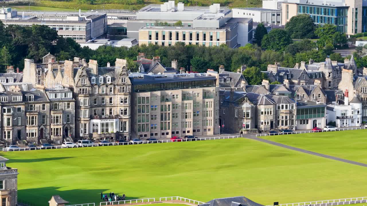 Drone shot reveals iconic golf course, historic buildings, and lush green fairway in bright daylight