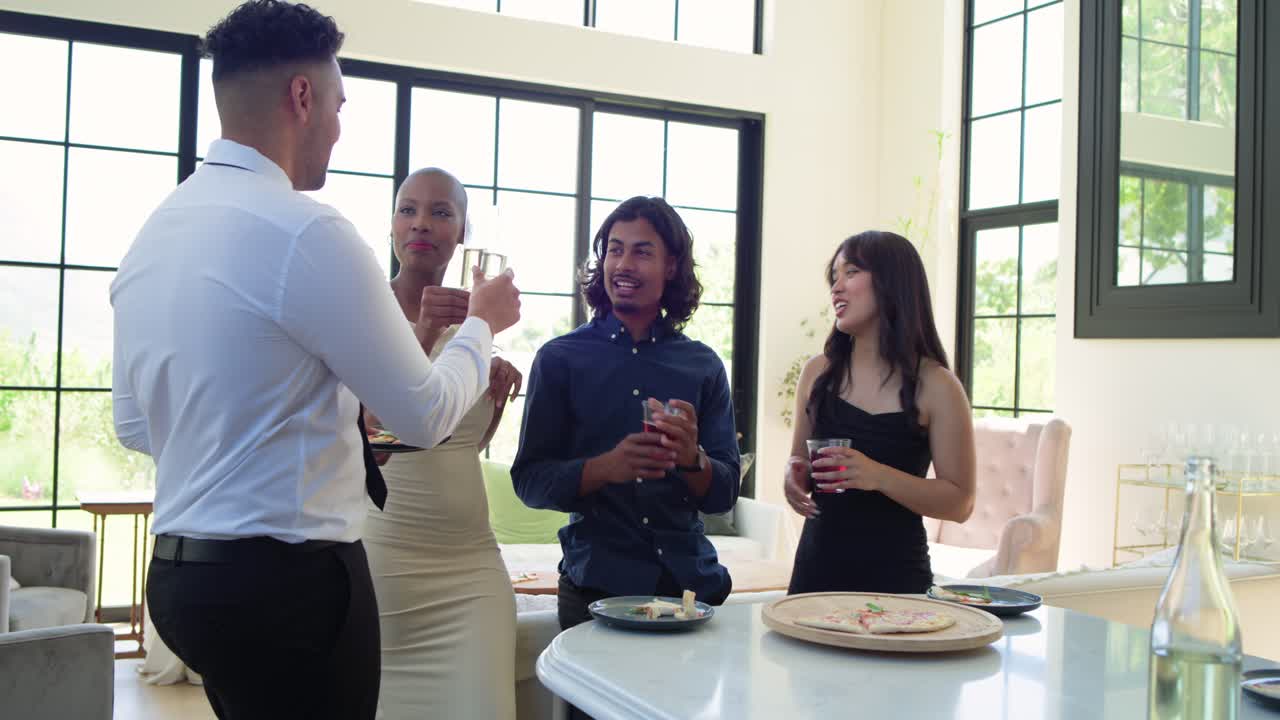 Diverse friends gathering at kitchen island after left man offering plate, raising glasses toasting