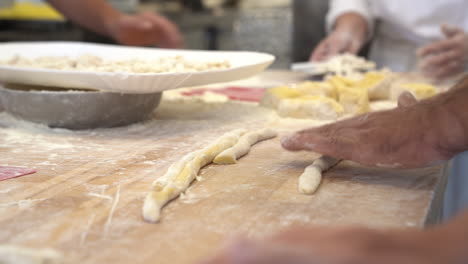 manos humanas, modelando y haciendo un tipo típico de pasta italiana sobre una mesa de madera con harina, agua y huevos