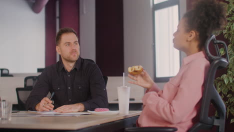 Side-View-Of-Pregnant-Woman-Sitting-At-Table-Talking-With-A-Coworker-In-A-Meeting-Room