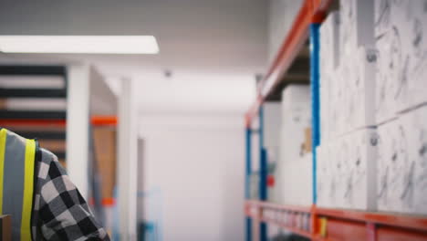 portrait of smiling young male worker wearing high vis safety vest holding box inside warehouse