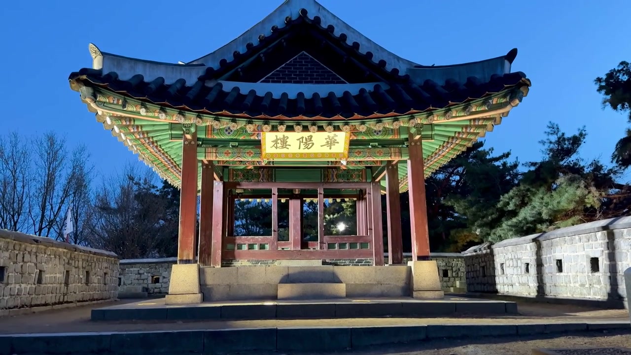 Vista notturna del Padiglione Hwayangnu presso la Fortezza di Suwon Hwaseong, con architettura tradizionale coreana illuminata, travi in legno dipinte e mura in pietra circostanti.