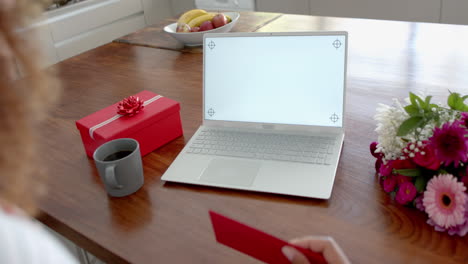 Biracial-woman-with-gifts-having-video-call-on-laptop-with-copy-space-screen,-slow-motion