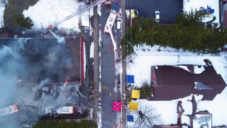 Luftaufnahme-Einer-Großen-Feuerlöschanlage-In-Einem-Industriegebäude,-Das-Immer-Noch-Raucht,-Während-Die-Feuerwehr-Weiterhin-Wasser-In-Den-Brand-Pumpt