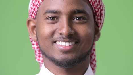 young handsome african man wearing traditional muslim clothes against green background
