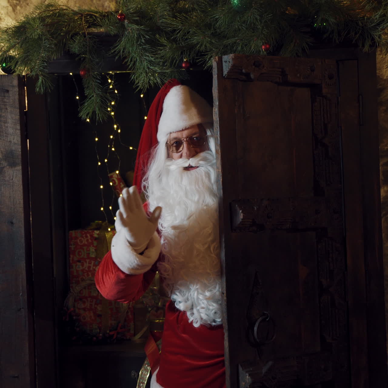 Santa look out from the door and waving hand in white glove. Wooden door and Santa Claus with white beard and eyeglasses making bye gesture. Christmas time.