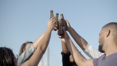 happy people clinking beer bottles against blue sky.