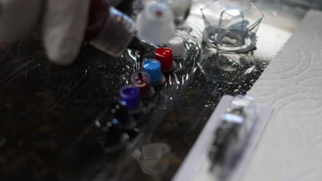 Tattoo artist filling ink cups with red maroon blue and black inks as close up shot focuses on reflection in sanitized shrink cling wrap and red color in background