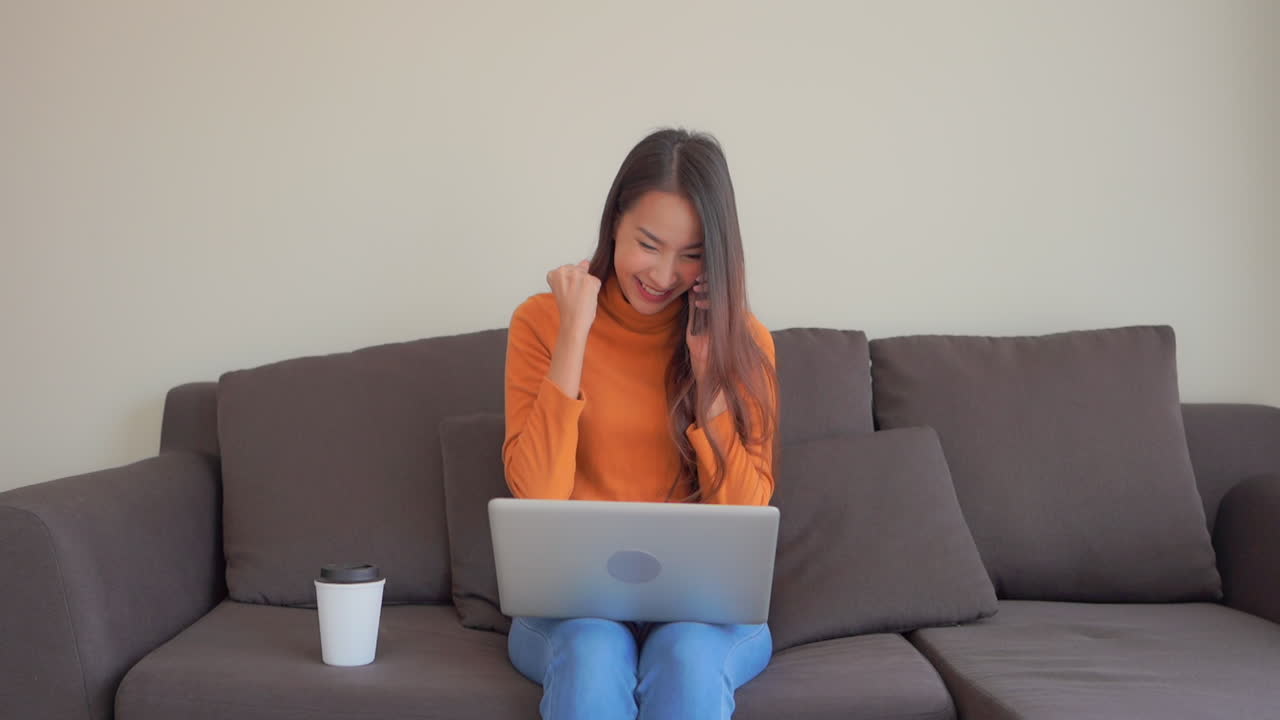 A young woman is on her smartphone talking while working on her laptop