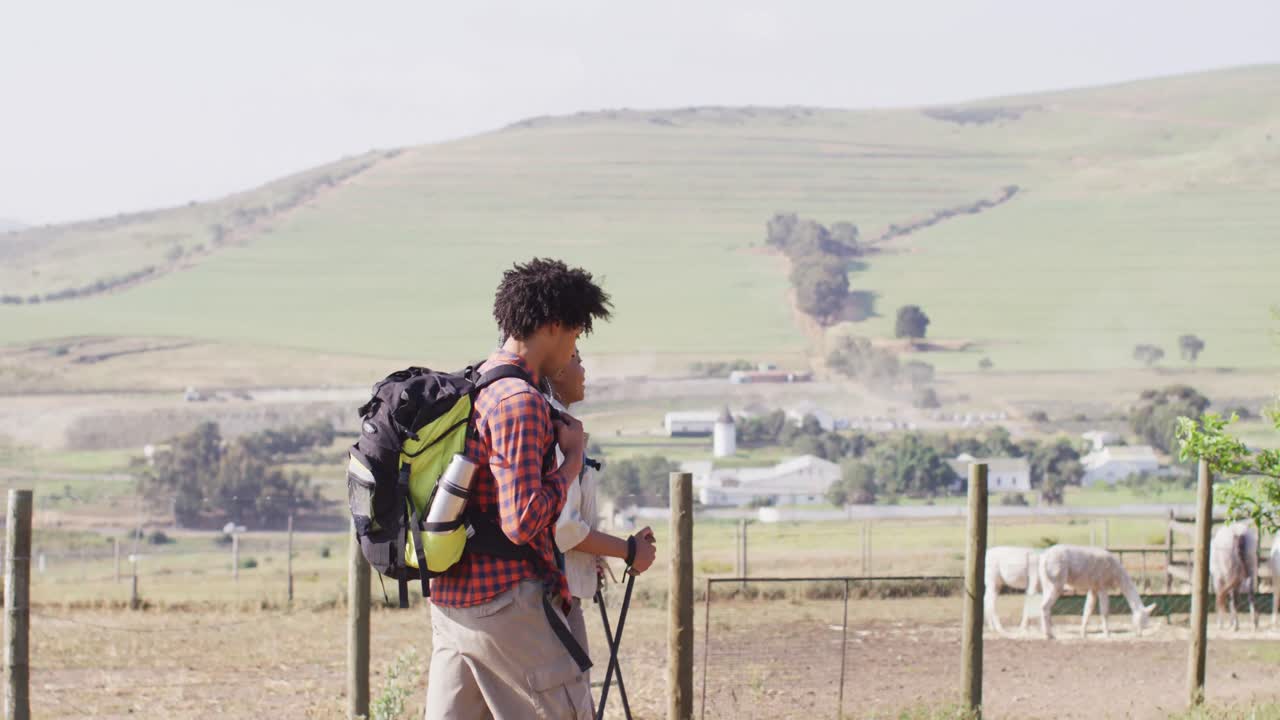 feliz pareja afroamericana con mochilas, caminando con palos de trekking juntos, cámara lenta