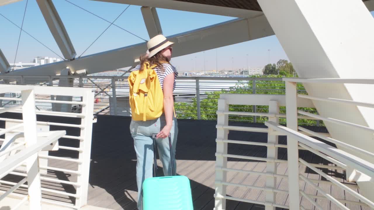 A woman wearing a yellow backpack is walking on a bridge