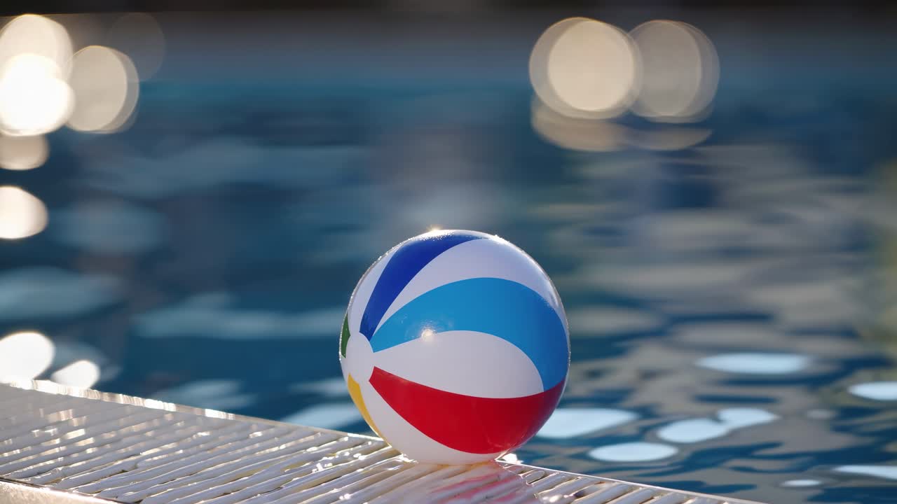 Un colorido balón de playa descansa junto a la piscina, reflejando la luz del sol, mientras las ondas del agua crean una atmósfera vibrante, mostrando una escena veraniega y divertida en movimiento.