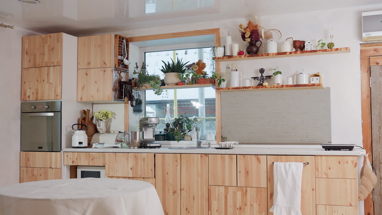 Beautiful modern kitchen interior with wooden cabinets, indoor plants, oven, blender, and stylish decor items on floating shelves near large window