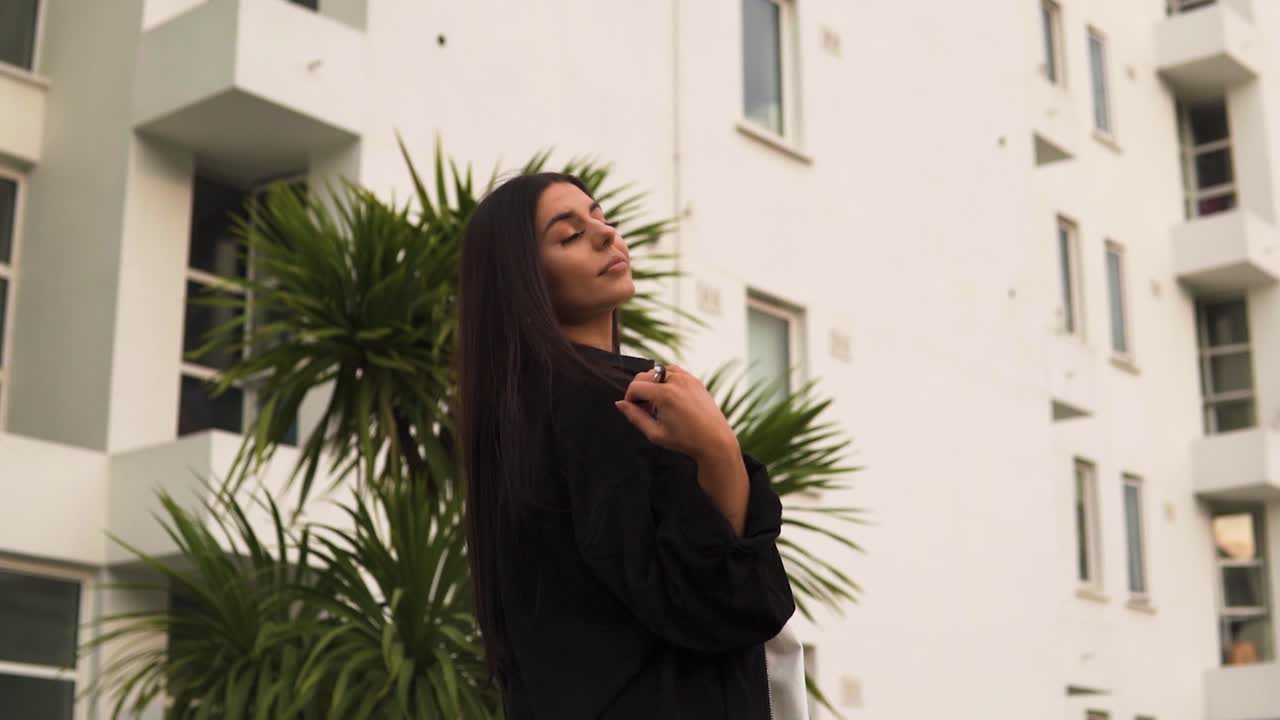 impresionante modelo caucásica con cabello largo para video musical caminando por el lugar de verano con plam árboles sonriendo mirando alrededor siendo descarado mostrando la lengua girando levantando sus manos puesta de sol en cámara lenta