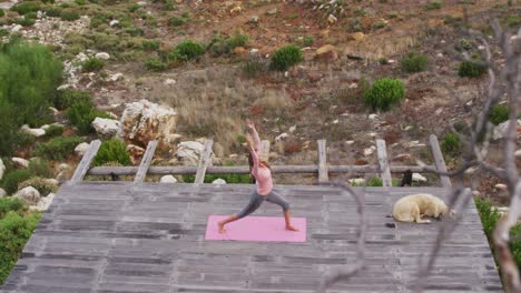 caucasian woman practicing yoga outdoors, stretching standing on deck in rural mountainside setting