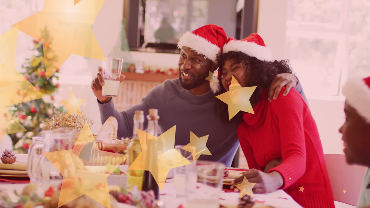 animación de estrellas cayendo sobre una feliz familia afroamericana con sombreros de papá noel y cenando
