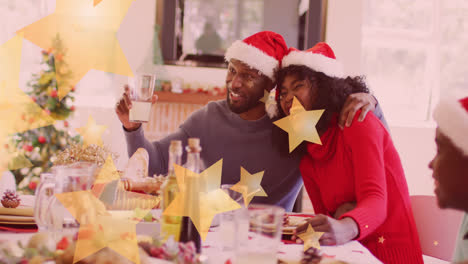 animation of stars falling over happy african american family wearing santa hats and having dinner