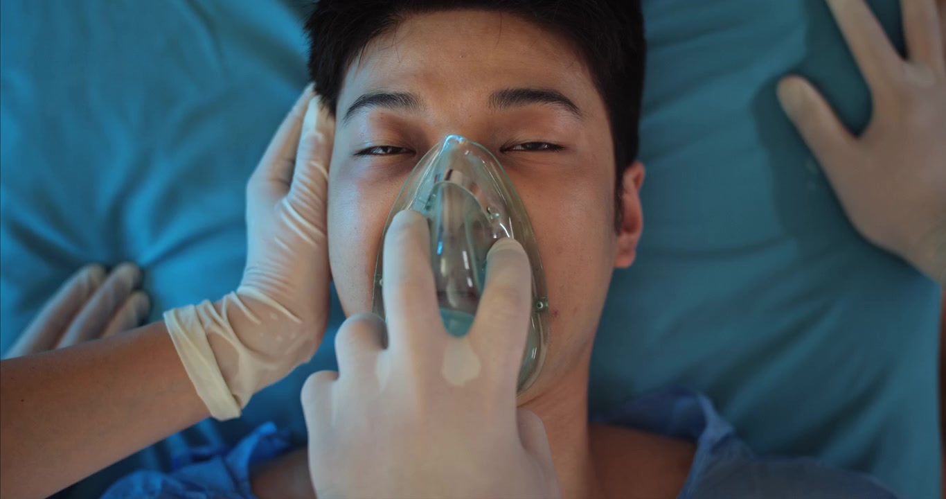 Professionista medico che applica una maschera per l'ossigeno a un giovane paziente maschio.