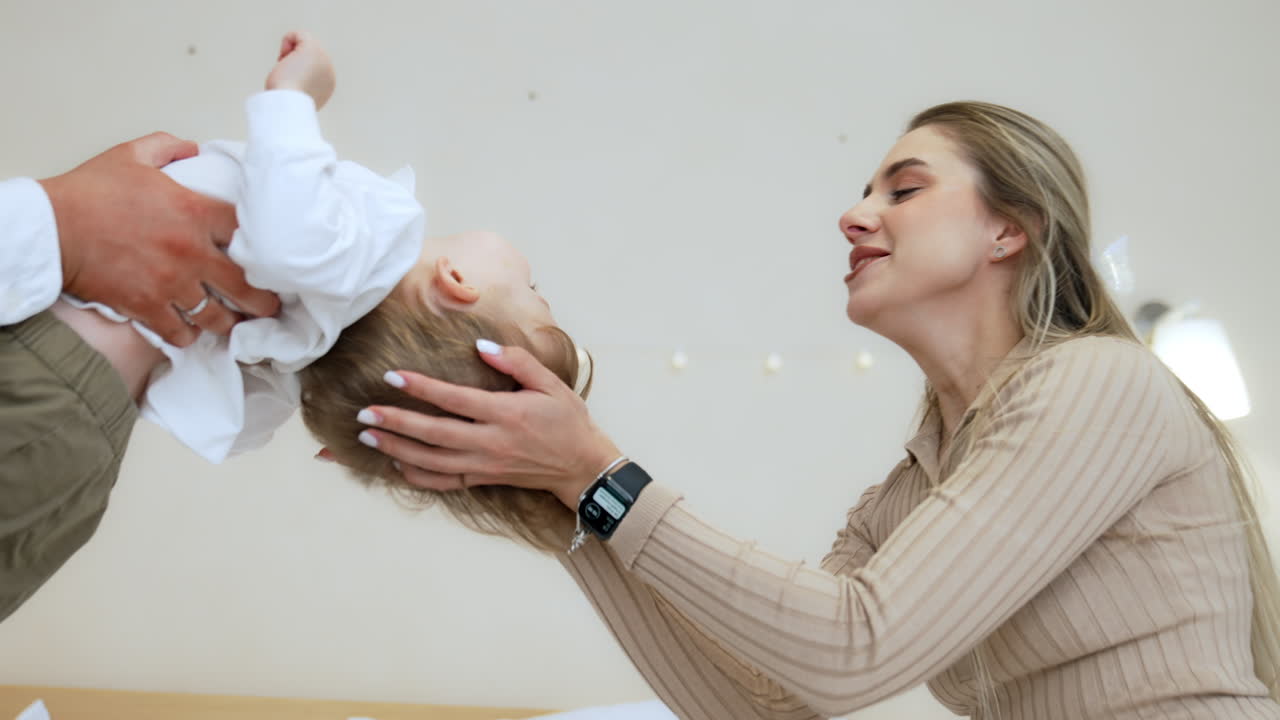 Man holding his baby boy bending back. Mother kisses her son on the forehead and dad kisses him on the tummy.