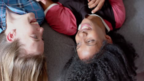 happy diverse female friends lying on bed and looking at each other at home, slow motion