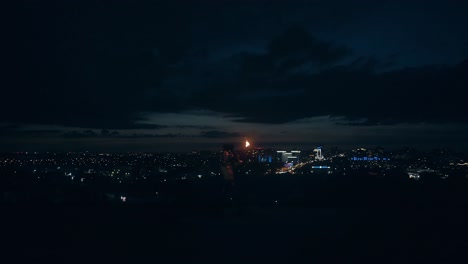 Young-blond-male-does-tricks-with-fire-breaths-fire-in-the-middle-of-the-night-with-city-skyline-in-the-background