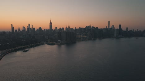 AERIAL:-Over-East-River-overlooking-Manhattan-New-York-City-Skyline-in-Beautiful-Dawn-Sunset-Orange-Light