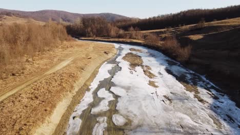 Drone-shot-of-the-forest-and-a-country-icy-river-in-the-late-autumn