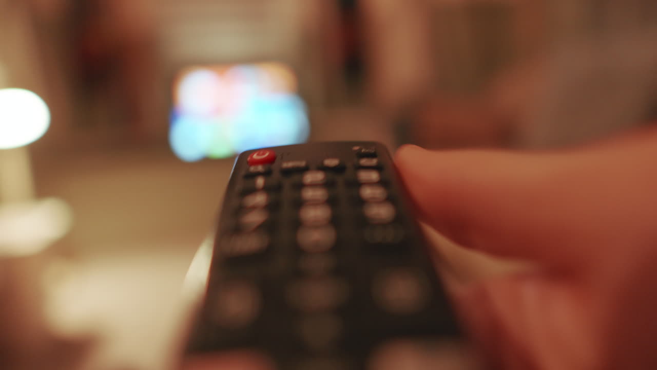 Mano che tiene il telecomando, spegnendo la TV, in un ambiente interno accogliente.